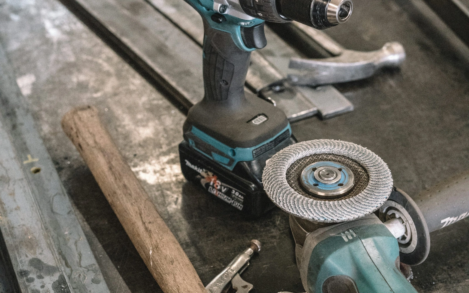 A cordless drill, angle grinder and hand tools on a steel workbench